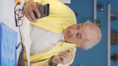 Vertical-video-of-Home-office-worker-old-man-rejoicing-on-the-phone.